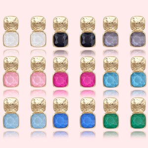 May include: A collection of gold-toned earrings with a textured top and a square, colored gemstone bottom. The earrings are available in white, black, gray, pink, fuchsia, light blue, blue, and green.