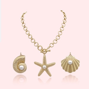 May include: Gold-toned necklace with a starfish pendant and two seashell charms. The necklace features a toggle clasp and a chain of connected circles. Each charm has a faux pearl center, creating a coastal theme.