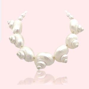 Könnte beinhalten: Eine weiße Muschelkette mit goldenen Akzenten. Die Kette besteht aus großen, weißen Muscheln, die mit goldenen Perlen aneinandergereiht sind.