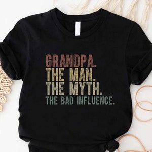 K&ouml;nnte beinhalten: Schwarzes T-Shirt mit einem Vintage-Grafikdruck, der "Grandpa. The Man. The Myth. The Bad Influence." lautet.