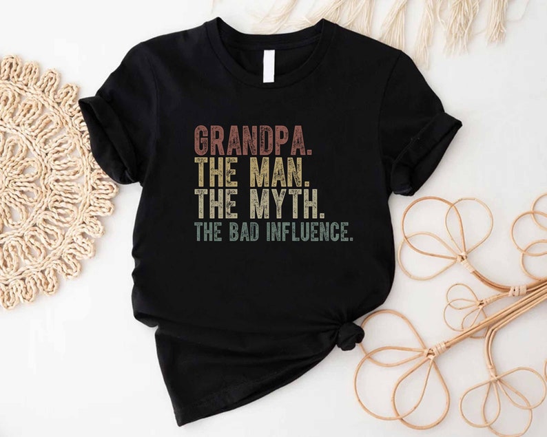 K&ouml;nnte beinhalten: Schwarzes T-Shirt mit einem Vintage-Grafikdruck, der "Grandpa. The Man. The Myth. The Bad Influence." lautet.