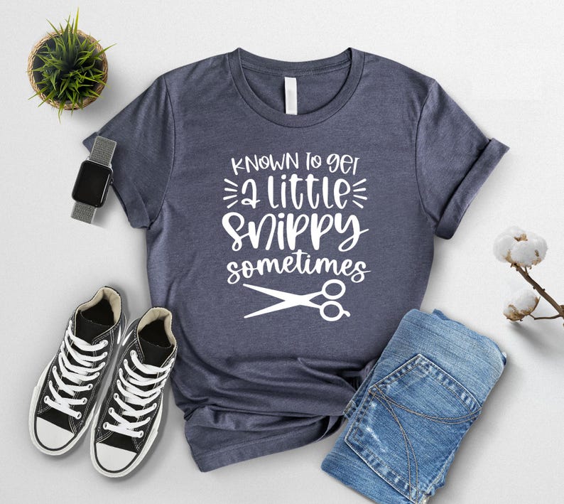 Pu&ograve; includere: Una maglietta blu navy con testo bianco che recita "Known to get a little snippy sometimes" e un paio di forbici bianche.