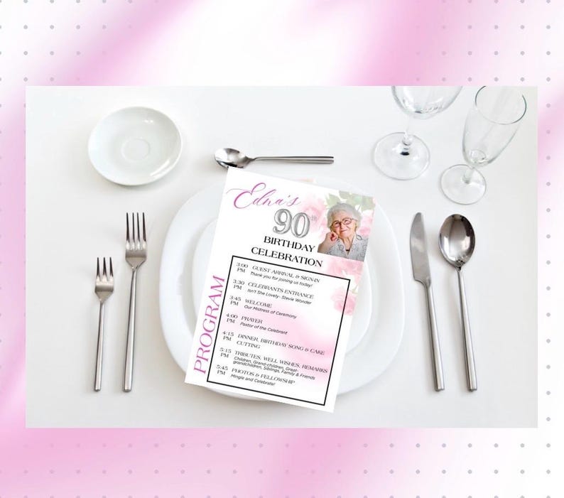 May include: A table setting with a white plate, silverware, and a printed program for Edna's 90th Birthday Celebration. The program includes a photo and schedule of events. Pink floral accents and a pink border frame the scene.