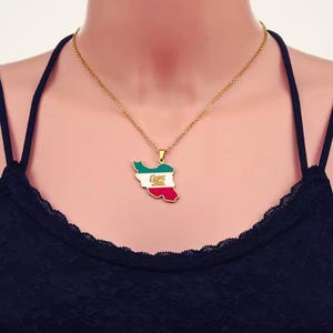 Puede incluir: Un collar dorado con un colgante con la forma de Irán. El colgante está coloreado con los colores verde, blanco y rojo de la bandera iraní, e incluye un emblema dorado. El collar lo lleva una persona.