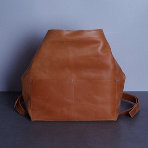 May include: A brown leather backpack with two large pockets on the front. The backpack has a simple design and is made of high-quality leather.
