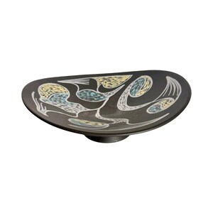 May include: A shallow, dark charcoal-colored bowl with an irregular, organic shape. The interior surface features a decorative pattern of white, pale yellow, and light blue abstract shapes and lines that contrast against the dark background.