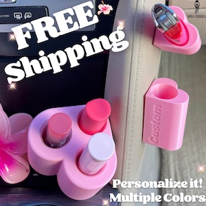 May include: Pink heart-shaped car organizer with three slots for lip balm or other small items. The organizer is attached to the back of a car seat. The text "Custom" is printed on the organizer. The text "Personalize it! Multiple Colors" is printed below the organizer.