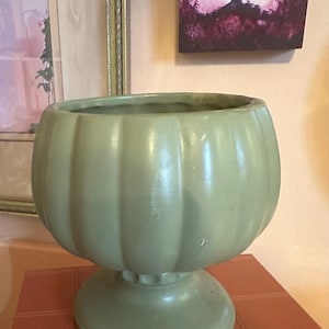 May include: A green ceramic planter with a fluted design and a pedestal base.