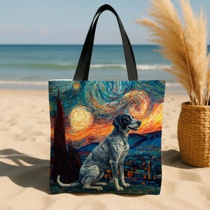 May include: Tote bag featuring a dog in a painting style reminiscent of Van Gogh's "Starry Night." The bag has a black handle and depicts a dog sitting in front of a town with a swirling, colorful sky. The background is a beach.