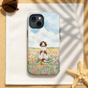 May include: A phone case featuring a painting of a dog sitting in a field of flowers under a blue sky with clouds. The dog is white with brown spots and is wearing a black collar. The case is on a white towel with sunglasses and a starfish.