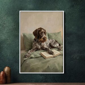 Pode incluir: Impressão emoldurada de um cão usando óculos, deitado em uma cama com um livro. O cão tem pelo marrom e branco e está descansando em um cobertor e travesseiros verdes. O fundo é de cor neutra.