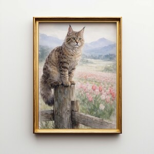 May include: A framed painting of a cat sitting on a wooden fence post, overlooking a field of pink flowers and distant mountains. The cat has brown and tan fur, with green eyes. The frame is gold.