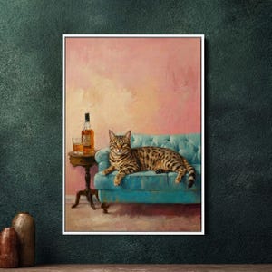 Op de afbeelding: Een ingelijst schilderij van een kat op een turquoise bank. Een tafeltje naast de bank heeft een fles drank en een glas. De achtergrond is zachtroze. De kat heeft bruine en zwarte vlekken.