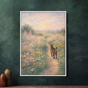 Op de afbeelding: Een ingelijst schilderij toont een tabby kat die een pad bewandelt door een veld met kleurrijke wilde bloemen. Het kunstwerk heeft een zachte, impressionistische stijl met een warm kleurenpalet van roze, geel en groen, onder een zachte zonsondergang.