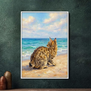 Op de afbeelding: Een ingelijst schilderij van een gevlekte kat die op een zandstrand zit en uitkijkt over de turquoise zee onder een blauwe lucht met wolken. Het kunstwerk is in realistische stijl, met gedetailleerde penseelstreken.