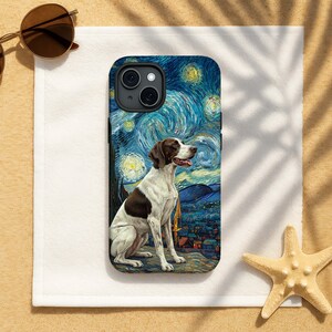 May include: A phone case featuring a brown and white dog sitting in front of a starry night sky, reminiscent of Van Gogh's painting. The case has a black border and is on a white surface with sunglasses and a starfish.