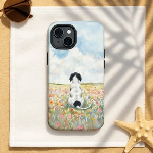 Könnte beinhalten: Handyhülle mit einem Aquarellgemälde eines schwarz-weißen Hundes, der in einem Feld bunter Blumen sitzt, mit blauem Himmel und Wolken im Hintergrund. Die Hülle liegt auf einem weißen Handtuch.