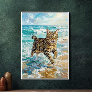 Op de afbeelding: Een ingelijst schilderij van een Bengaalse kat die door oceaangolven op een zandstrand rent. De kat heeft een gevlekte vacht van bruin, zwart en bruin. De lucht is blauw met witte wolken en het water is turquoise.