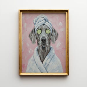 Op de afbeelding: Een ingelijst schilderij van een Weimaraner-hond met een badjas en handdoek, met komkommerschijfjes op de ogen. De achtergrond is roze en het frame is goudkleurig.