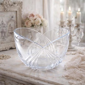 May include: A clear, decorative glass bowl with a unique, curved design. The bowl features a fan-like pattern radiating from the base. The bowl is displayed on a white surface, with candles and flowers in the background. A perfect centerpiece for any table.