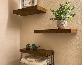 May include: Three wooden shelves with a wire basket shelf. The top shelf has a white framed sign with the text "Worn. Enjoy. Tomorrow. You." The middle shelf has a small potted plant with green leaves. The bottom shelf has two blue bird figurines.