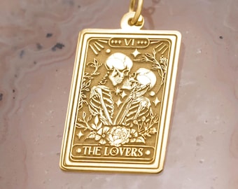 May include: Gold-colored pendant necklace featuring a rectangular charm with a tarot card design. The charm depicts two skeletons embracing, with the words "THE LOVERS" at the bottom. The necklace is on a gold chain.