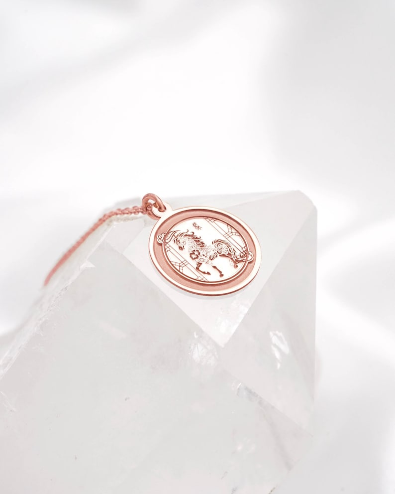 14k rose gold lunar new year horse necklace styled in a bright flatlay to show shine, chain drape, and the round coin silhouette. The Year of the Horse is associated with bold independence and lucky new starts in Chinese zodiac lore, making it a thoughtful keepsake. SEO search terms: rose gold horse necklace, chinese zodiac charm, year of the horse pendant, astrology jewelry, minimalist medallion necklace, free engraving gift.