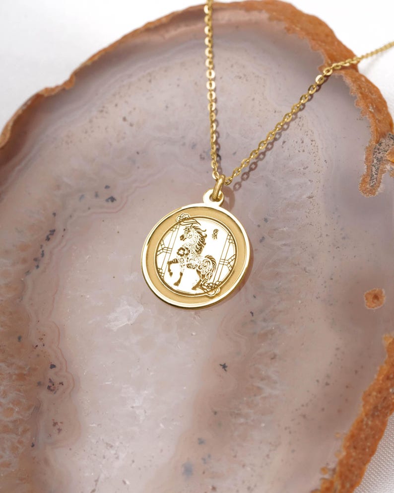 14k solid gold lunar new year horse necklace close-up showing a shiny round medallion pendant, raised border, and delicate cable chain. The Horse is linked to ambition, independence, and good fortune in Chinese zodiac traditions, making this a thoughtful birthday or New Year present. Handcrafted and finished by hand; offered with multiple pendant sizes and chain lengths. Search phrases: Chinese zodiac necklace, horse pendant, year of the horse jewelry.
