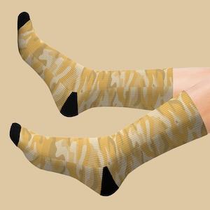 May include: A pair of socks with a beige and white abstract pattern. The socks have black heels and toes.