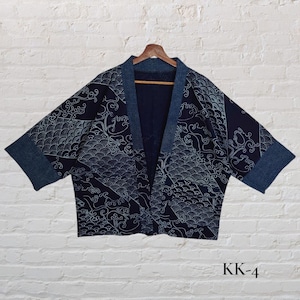 May include: Navy blue kimono-style jacket with a wave pattern in light blue and white. The jacket has a denim-like trim and short sleeves. The text "KK-4" is visible in the lower right corner. The jacket is hanging on a wooden hanger.
