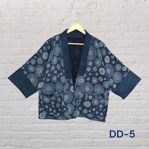 May include: A navy blue kimono-style jacket with a white circular pattern. The jacket has a shawl collar, two pockets, and wide sleeves. The sleeves and collar are a darker shade of blue. The text "DD-5" is visible in the lower right corner.