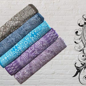 May include: Rolled fabric rolls in shades of brown, blue, turquoise, and purple, each with a unique geometric pattern. A black and white decorative floral design is on the right side of the image. The fabric rolls are stacked diagonally.