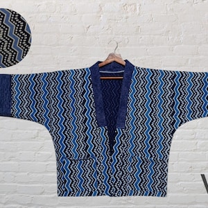 Puede incluir: Un cárdigan azul y blanco con estampado de kimono, cuello en V y mangas largas. El cárdigan tiene un patrón de chevron y está hecho de una tela suave y ligera.