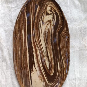 May include: Oval-shaped ceramic serving dish with a marbled pattern in shades of brown and beige. The dish has a glossy finish and a slightly raised rim. The design resembles natural stone or wood grain.