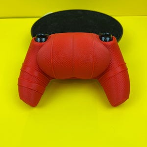 May include: Red silicone controller cover for a gaming console. The cover has a textured surface and is designed to fit snugly over the controller.