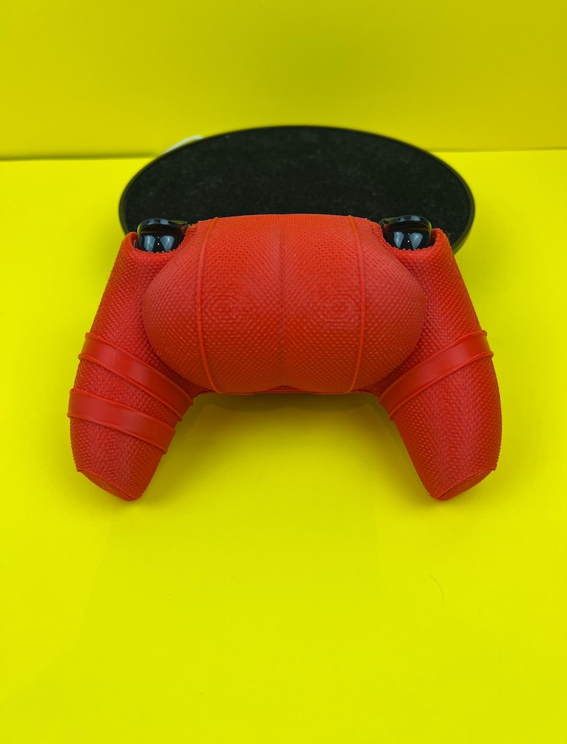 May include: Red silicone controller cover for a gaming console. The cover has a textured surface and is designed to fit snugly over the controller.