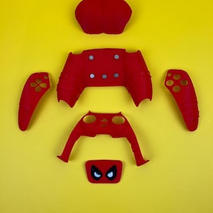 May include: Red and black video game controller faceplate with a spider-man design. The faceplate is made up of six separate pieces, including the front, back, and two side panels.