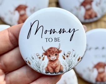 May include: White round button with the text "Mommy TO BE" in black script. The button features a watercolor illustration of a Highland cow calf with brown fur and horns, surrounded by floral elements.