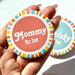 May include: Two round buttons with the text "Mommy to be" and "Daddy to be". The "Mommy to be" button is coral with a colorful border. The "Daddy to be" button is light blue with a colorful border.