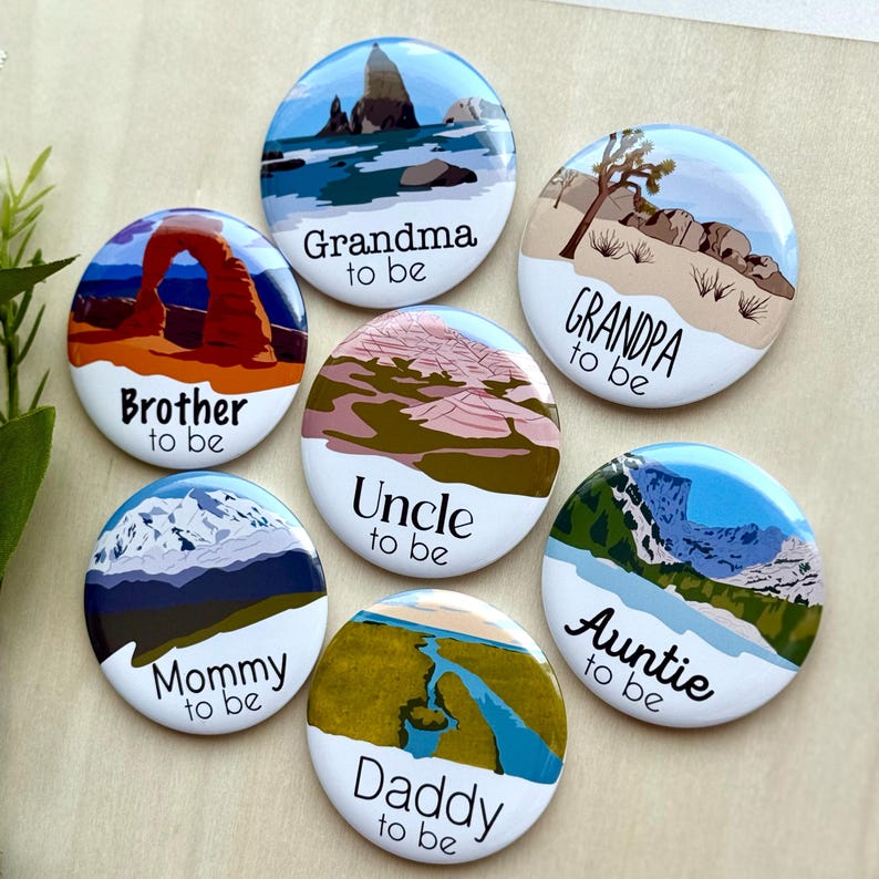 May include: A collection of seven round, white buttons with colorful landscape illustrations. Each button has a different title, including "Brother to be," "Grandma to be," "Mommy to be," "Uncle to be," "Grandpa to be," "Daddy to be," and "Auntie to be."