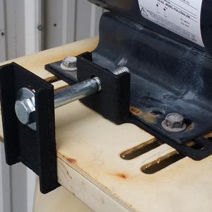 May include: A close-up of a black metal bracket with a silver bolt and nut. The bracket is attached to a wooden surface.