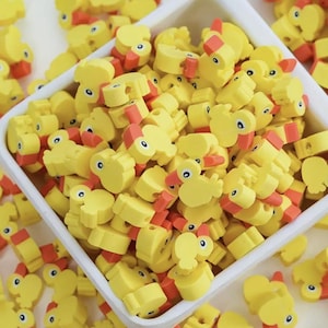 May include: A bowl filled with yellow rubber ducky shaped beads with orange beaks. The beads are small and perfect for crafting.