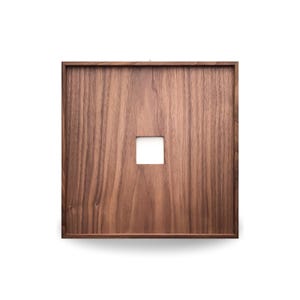 Puede incluir: Una pieza de arte mural cuadrada de madera con un acabado marrón oscuro. La veta de la madera es visible. Una pequeña abertura cuadrada blanca está centrada en la obra de arte. La pieza está diseñada para colgarse en una pared.