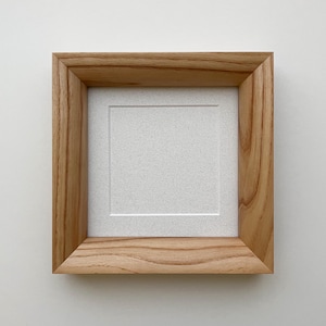 Puede incluir: Marco de fotos cuadrado de madera clara. El marco tiene un paspartú blanco y una abertura cuadrada. La veta de la madera es visible. Diseñado para contener una foto o una obra de arte cuadrada.