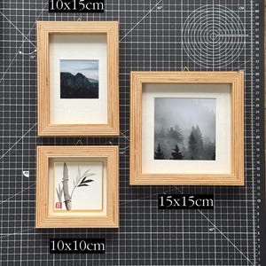 May include: Three wooden picture frames of varying sizes: 10x10cm, 10x15cm, and 15x15cm. Each frame holds a different black and white image. One shows a mountain range, another a forest, and the third a bamboo plant. The frames are on a black cutting mat.