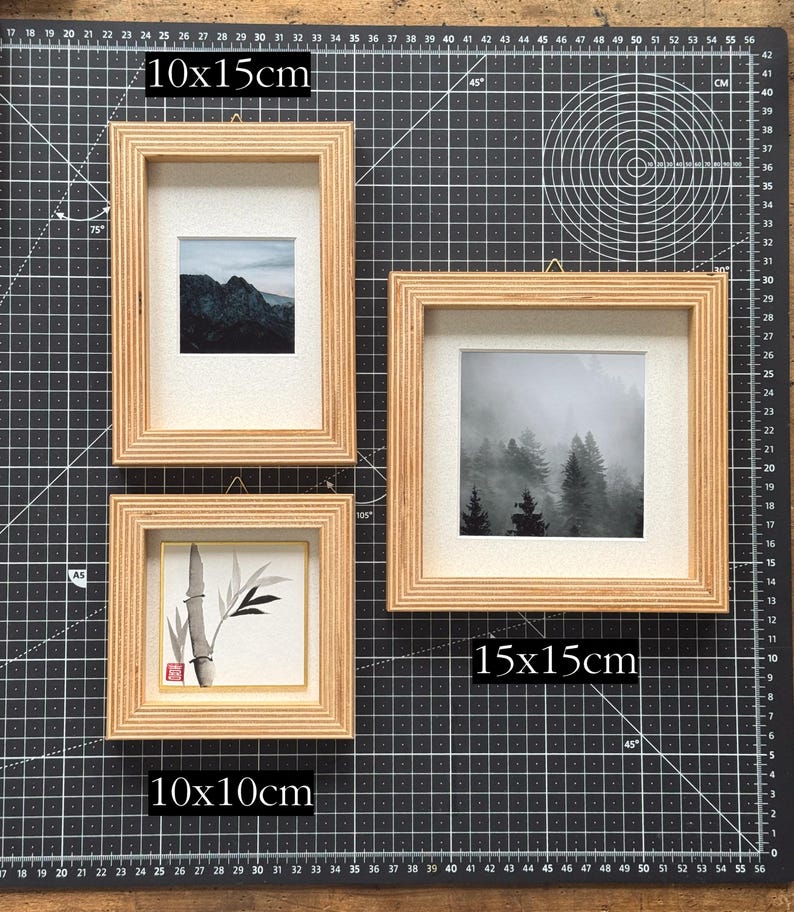 May include: Three wooden picture frames of varying sizes: 10x10cm, 10x15cm, and 15x15cm. Each frame holds a different black and white image. One shows a mountain range, another a forest, and the third a bamboo plant. The frames are on a black cutting mat.