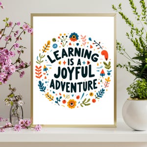 May include: A gold framed print with a white background and a colorful floral circle design. The text inside the circle reads "Learning is a Joyful Adventure".