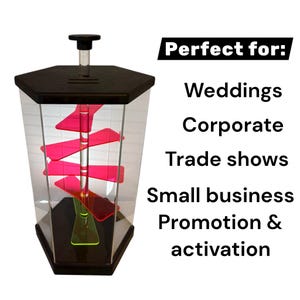 Puede incluir: Una vitrina hexagonal transparente con tapa y base negras. En el interior, un poste central sostiene varios estantes rosas brillantes y en &aacute;ngulo. Se muestra el texto "Perfect for: Weddings, Corporate, Trade shows, Small business Promotion & activation".