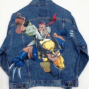 May include: A blue denim jacket with a painted image of Wolverine and Ryu from Street Fighter. Wolverine is in the foreground, with Ryu in the background.