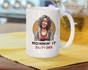 Peut inclure: Une tasse en céramique blanche avec une illustration de dessin animé d'une femme aux cheveux bruns et une chemise rouge. Le texte "Mommin' It 24/7.365" est imprimé sur la tasse.